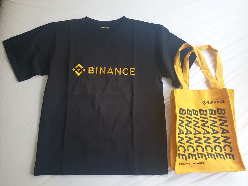 A black Binance-branded T-shirt and a yellow Binance tote bag