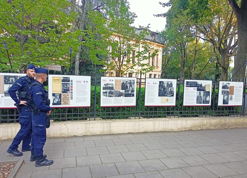 Two police officers walk past an outdoor exhibition at the fence of the Constitutional Tribunal in Warsaw